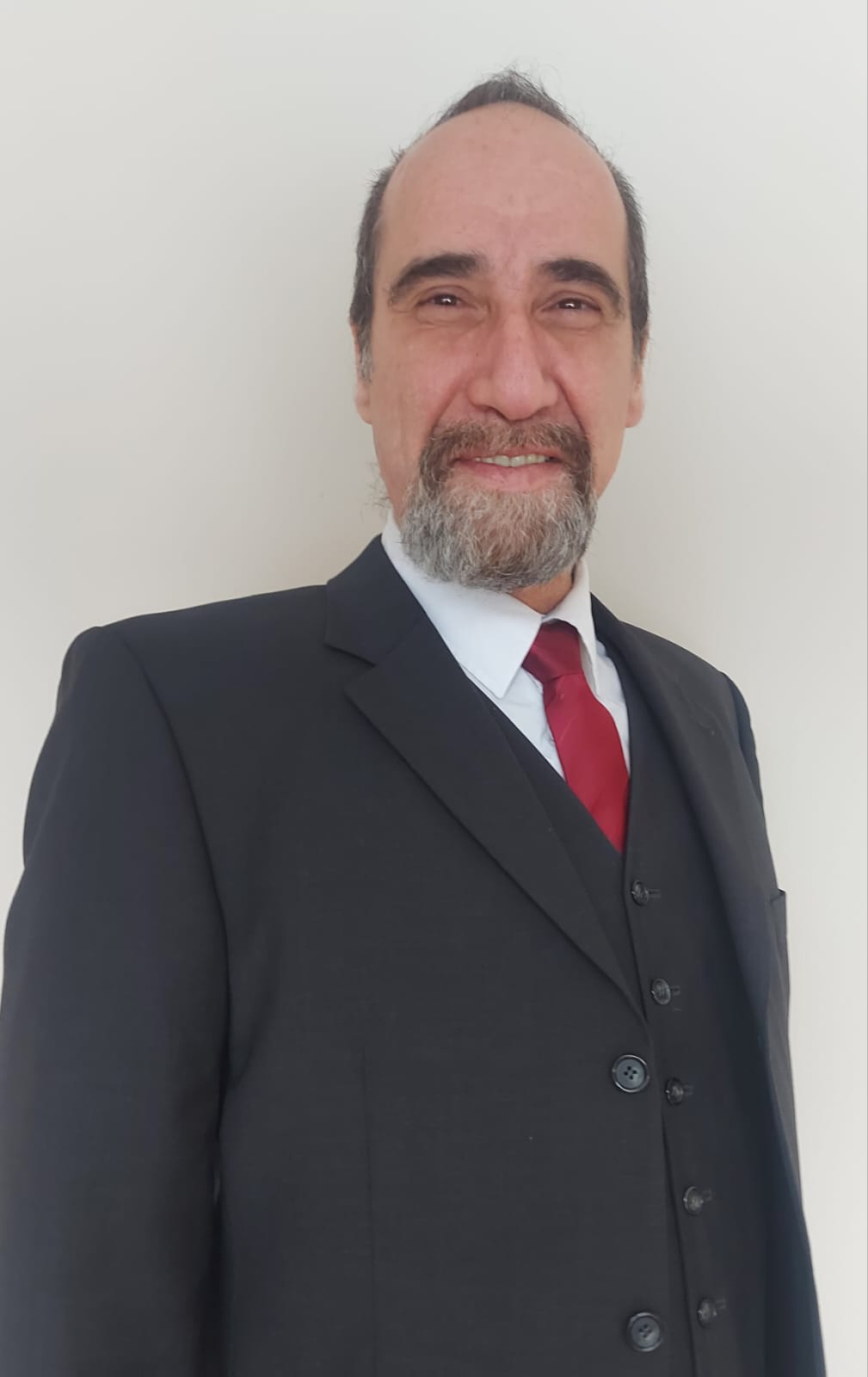 رجل بلحية وشعر قصير يرتدي بدلة سوداء وربطة عنق حمراء ويبتسم ابتسامة خفيفة